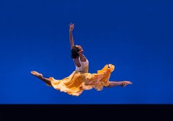 photo of dancer leaping through air with skirt contrasting with blue background