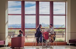 Three students sitting by large window in CELS building overlooking the NY skyline.