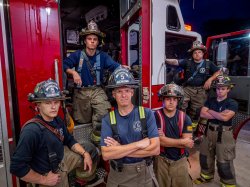 group of firefighters posed on the back of a hook-and-ladder truck