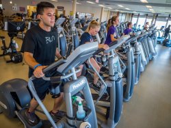 Photo of students in a gym working out on elliptical machines