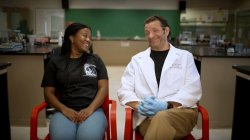 Student and professor sit in red chairs in a science lab.