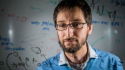 A man looks through a glass plate covered with physics equations.
