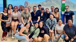 Group of students pose with mountain, sea in background.