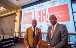 Two men pose for a photo in front of a slide presentation.