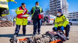 Three paramedics in reflective vests over man on stretcher with ambulance in background
