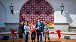 A woman holding a pair of oversized scissors is flanked by three women and a man.