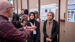 A man talks to two students in hijab about their research poster about annotating the genomes of sea phages.