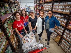 Five women stand with a shopping cart in an aisle of canned goods.