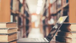 Open laptop on table in school library among old stacks of textbooks.