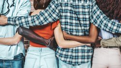 A group of young adults facing away from camera stand shoulder-to-shoulder