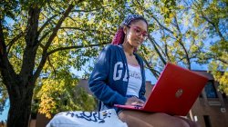 student with laptop sitting under tree