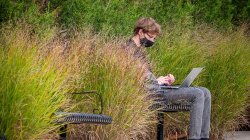 Person sitting outside on a bench, wearing a mask.