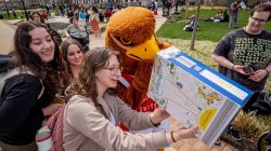 Students and a mascot look in a cereal box made as a solar pinhole viewer.