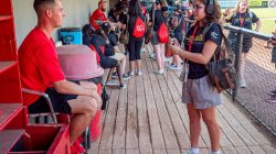 A student interviews a baseball player in a dugout.