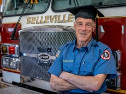 Ralph Castellano celebrates his Montclair State University graduation at the Belleville Fire Department, wearing his uniform and graduation cap.