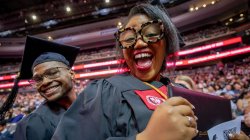 Two graduates in caps and gowns smile for the camera