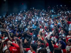 Hundreds of students hold their phone lights up in the air.