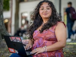 Sara Flores sitting on campus with her laptop open.