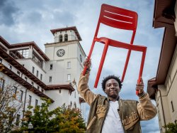 Student taking a picture holding the signature red chair above his head.