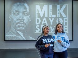 Two sorority members stand before a Martin Luther King Jr.’s Day of Service screen.
