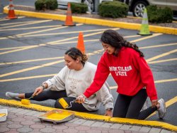 Two girls repainting yellow lines on the road