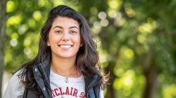 Woman wearing montclair shirt under jacket smiling to camera in front of soft-focus greenery
