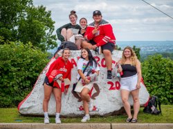 Six high school students posing on a boulder with Montclair State University gear on.