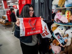 Student smiling while her picture is being taken. She is holding up a flag with the Red Hawk mascot, with the words "Go Red Hawks." written on it.