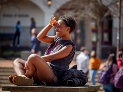 Photo of a female student sitting on a campus with her hand up shielding her eyes from the sun