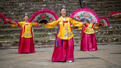 Three dancers wearing traditional Korean dress and with large fans.