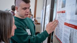 A student discusses his research poster with a faculty member.