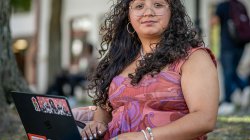 Sara Flores sitting on campus with her laptop open.