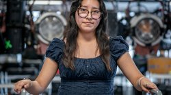 Pamela Hernandez stands in a campus broadcast media lab, surrounded by professional studio lights and equipment.