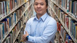 Kaung Hla Zan stands between two long shelves of books in a library.