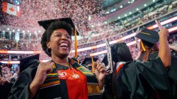 Graduate in cap and gown cheering as red and white confetti fills the air during Montclair State University’s 2026 Spring Commencement at Prudential Center.