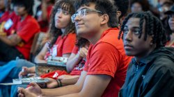 Franco Leon, wearing a red EOF T-shirt sits with hands clasped, smiling and looking up attentively during a conference session.