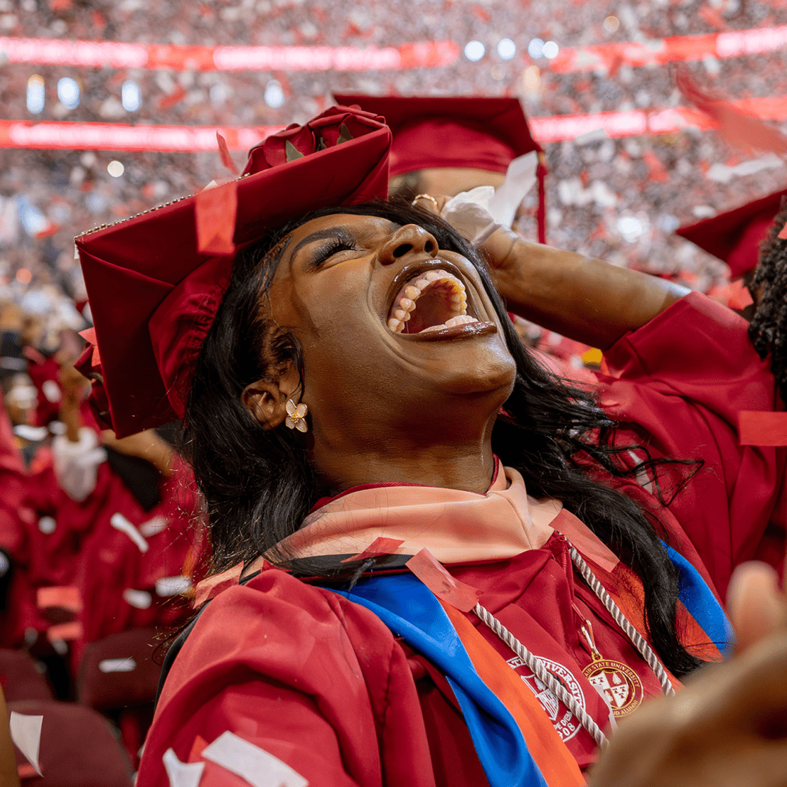 master's graduate student in red cap and gown smiling with confetti falling around them