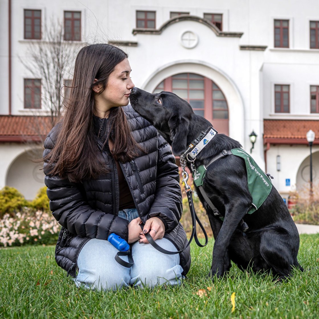 A woman student snuggles with a seeing-eye dog in training