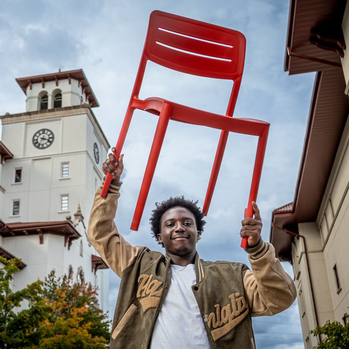 Student holds a red chair high over his head.