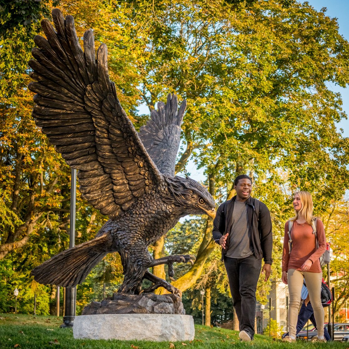 Two students walk on campus next to the Red Hawk statue.