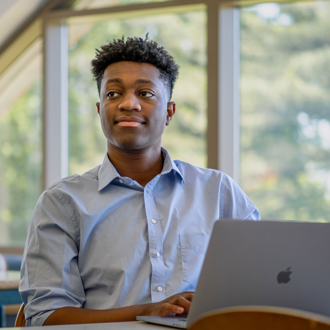 Student seated at table, looking up from laptop in front of them.