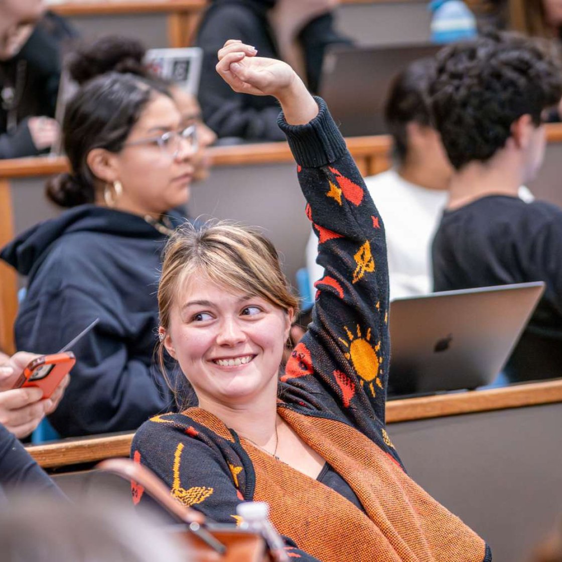 Student in classroom with hand raised.