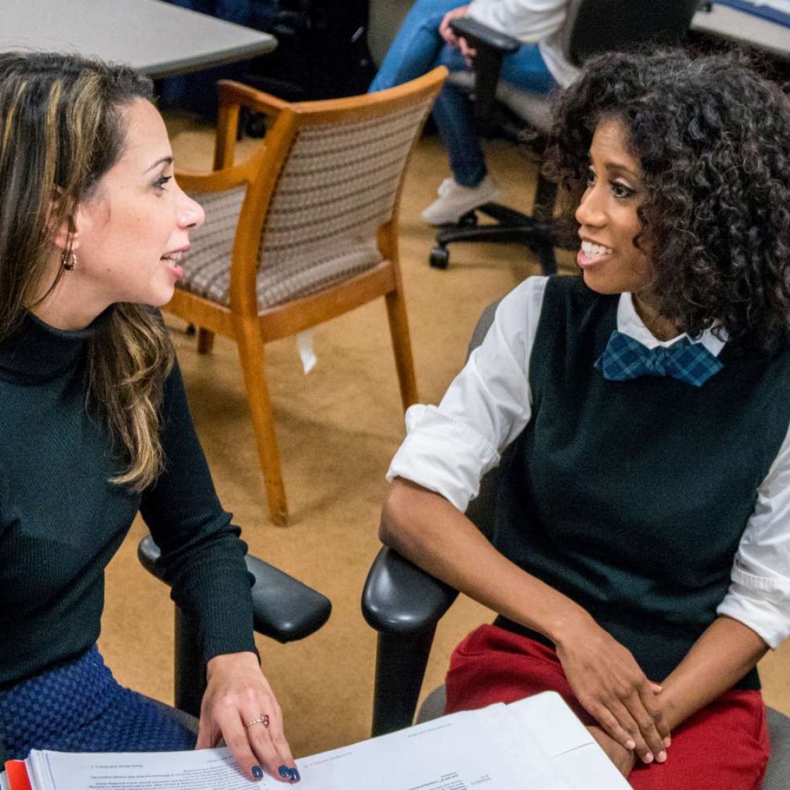 Two graduate students speaking, one holding a binder open between them.