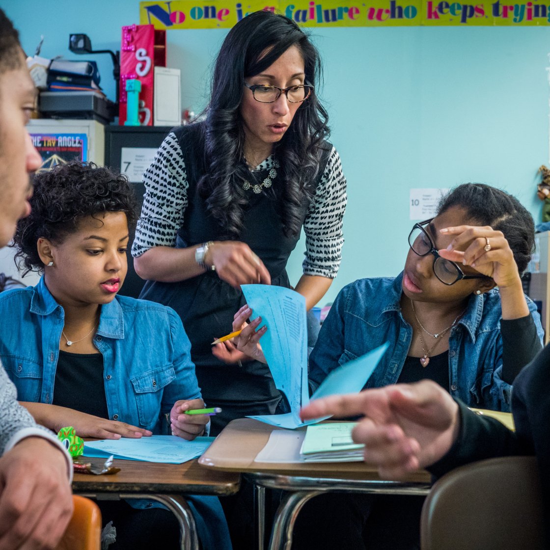 Teacher is explaining material in between two students at their desks.