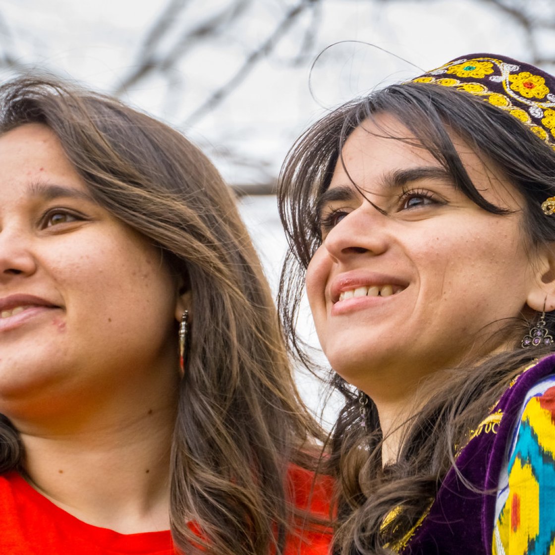 Two students stand side by side outdoors, one wearing a brightly patterned traditional outfit and headpiece.