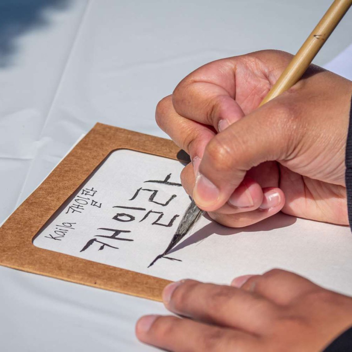 close-up of a hand holding a brush pen, writing in Hangul.