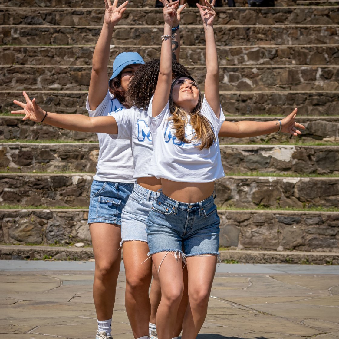 Three women are lined up gesturing their hands. 