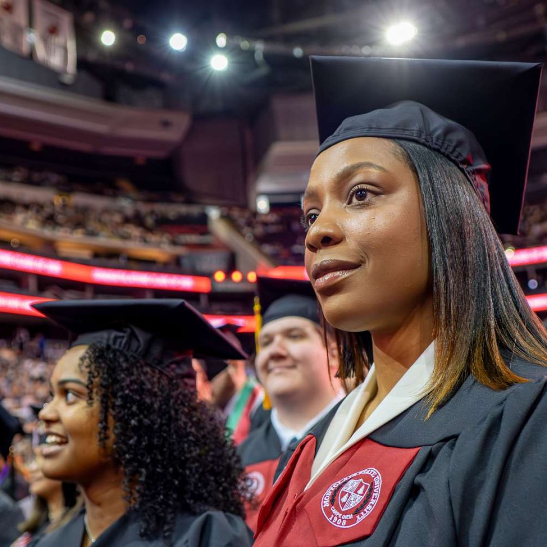 Student wearing cap and gown, seated at graduation ceremony.
