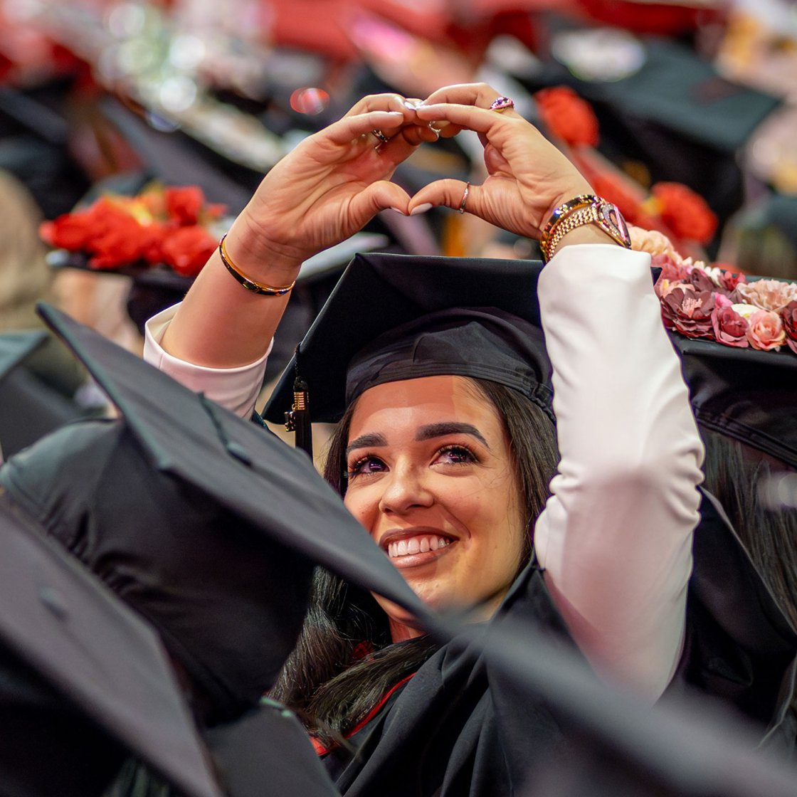 A graduate smiles and holds up their hands in the shape of a heart