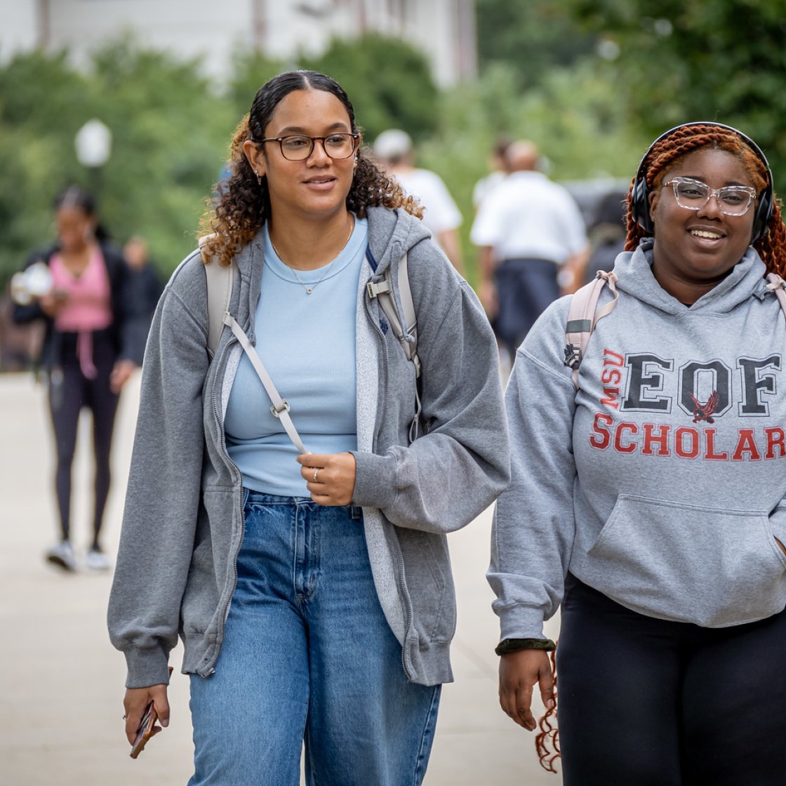 Two students walking together on campus, with one wearing a sweatshirt that has “EOF” printed on the front.